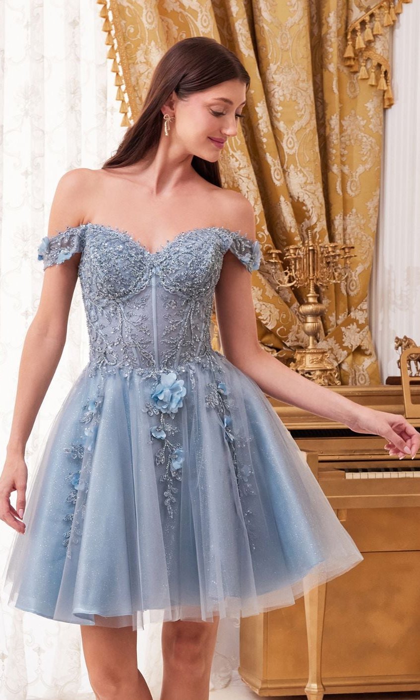 A woman in the Off-Shoulder Short Floral Homecoming Dress CD0194, featuring 3-D floral details, stands before a gold piano and ornate curtains, looking down and smiling.